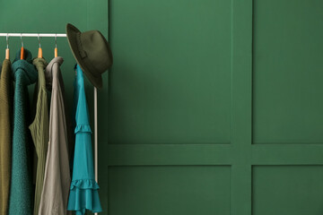 Rack with clothes and hat near green wall