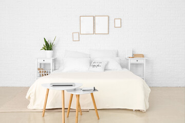 Interior of light bedroom with blank frames and tables