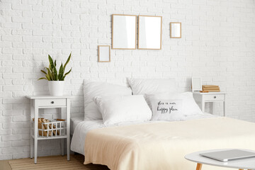 Interior of light bedroom with blank frames and tables