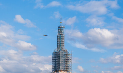 A passenger plane flying over the skyscraper on a summer day.