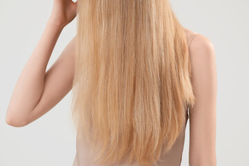 Fototapeta premium Blonde woman touching long hair on light background, closeup