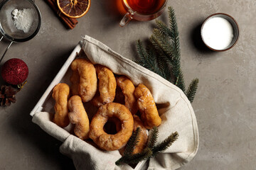 A wooden tray with donuts on a gray background, with fir branches, a cup with a drink and Christmas toys. Top view