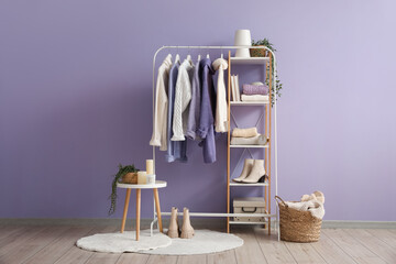 Rack with knitted sweaters and shelving unit near color wall in room