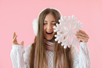 Happy young woman in warm ear muffs with big snowflake on pink background