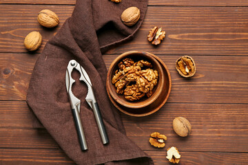 Bowl of walnut kernels and nutcracker on wooden background