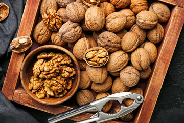 Wooden box with fresh walnuts and nutcracker on dark background, closeup