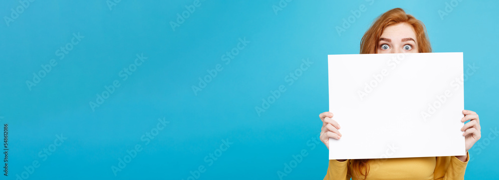 Wall mural Close up Portrait young beautiful attractive ginger red hair girl smiling showing blank sign. Blue Pastel Background. Copy space.