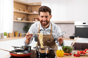 Glad adult european bearded male chef in apron prepare pasta in kitchen interior at table with...