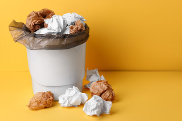 Rubbish bin with crumpled paper on yellow background