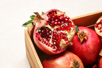 Wooden box with fresh pomegranates on light background, closeup