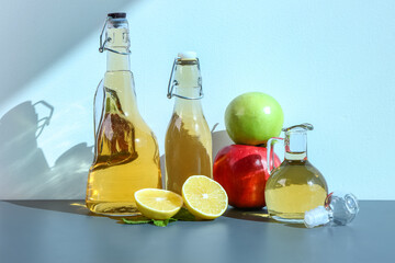 Bottles of apple cider vinegar and fruits on color background