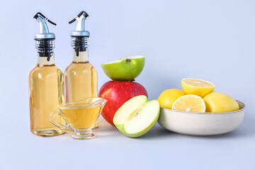 Bottles of apple cider vinegar and fresh fruits on light background