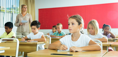 Fototapeta na wymiar Attractive smart preteen girl studying in classroom, listening to teacher and writing in notebook
