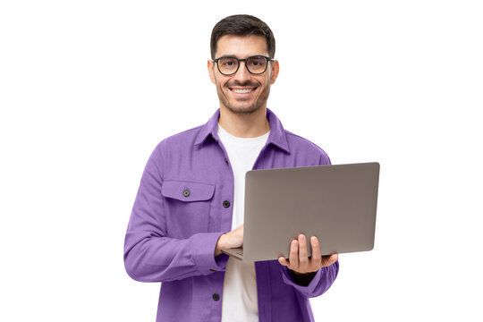 Studio portrait of young man standing holding laptop and looking at camera with happy smile