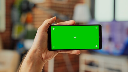 Male worker holding telephone with horizontal greenscreen template on digital screen, looking at isolated display. Using blank chroma key copyspace and mockup on smartphone. Close up.