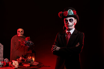 Smiling young adult wearing santa muerte costume in studio, having skull make up with black and white. Celebrating day of the dead mexican halloween tradition, festival horror look.