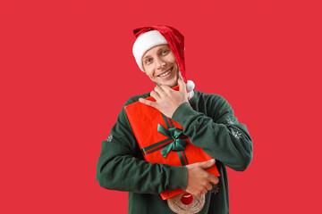 Handsome man in Santa hat with Christmas present on red background