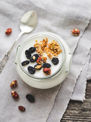Natural homemade yogurt in a glass jar. Healthy food for breakfast with muesli or granola. Jar with sour cream on linen tablecloth on wooden table.