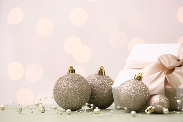 Christmas balls with gift and beads on table against blurred lights