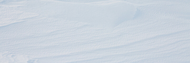 Beautiful winter background with snowy ground. Natural snow texture. Wind sculpted patterns on snow surface. Wide panoramic texture for background and design.