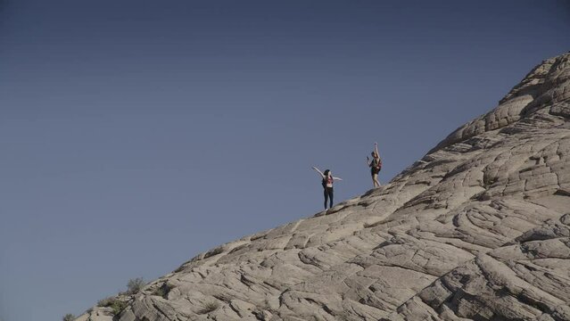 Slow motion of distant teenage girls photographing backpacking friend on mountain / Snow Canyon, Utah, United States