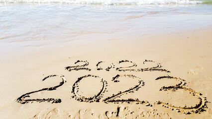 the inscription on the sand on the beach 2022 2023 is washed away by a wave. christmas at sea