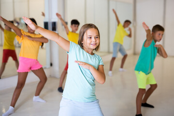 Happy tween girl dancing with children during group class in modern choreographic studio.