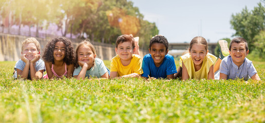 Group of school children resting on grass and smiling together in park