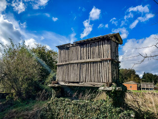 An old granary made of wood and stone stands alone in a village on a sunny day. Old granary on the Camino de Santiago. Galicia