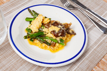 Fototapeta premium Scrambled eggs with mushrooms and asparagus served on plate with silverware.