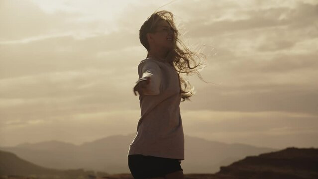 Slow motion of portrait of smiling teenage girl spinning in desert at sunset / St. George, Utah, United States