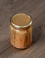 Preserved tuna fish fillets in a glass jar. Isolated on a wooden background