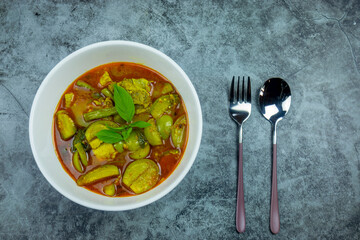 Yellow chicken curry with thai eggplant and sprinkle basil in a white bowl.