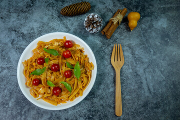 Pasta fettuccine with ketchup pepper topping small tomato and basil leaves served on top a dark gray stone table.