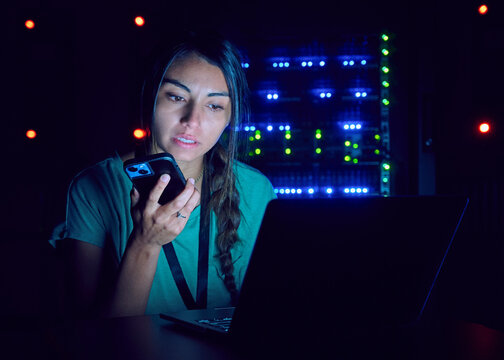 Female technician using laptop and smart phone in server room