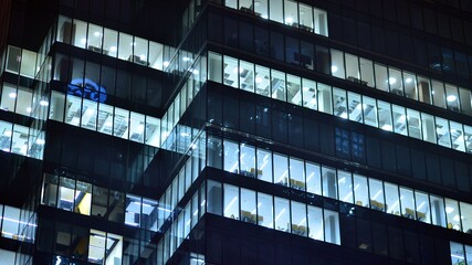 Obraz premium Modern office building in city at the night. View on illuminated offices of a corporate building. Blinking light in window of the multi-storey building of glass and steel. Long exposure at night