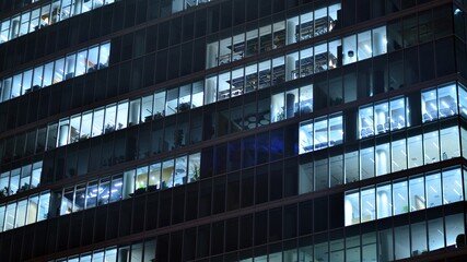 Fototapeta premium Modern office building in city at the night. View on illuminated offices of a corporate building. Blinking light in window of the multi-storey building of glass and steel. Long exposure at night