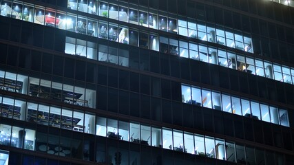 Obraz premium Modern office building in city at the night. View on illuminated offices of a corporate building. Blinking light in window of the multi-storey building of glass and steel. Long exposure at night