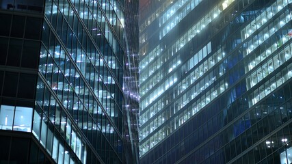 Modern office building in city at the night. View on illuminated offices of a corporate building. Blinking light in window of the multi-storey building of glass and steel. Long exposure at night