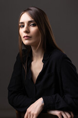 Naklejka premium Portrait of a young brunette with long hair in the studio. Dramatic photo in dark colors.