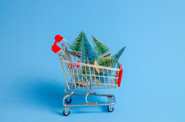 Shopping cart miniature with artificial small Christmas trees inside. Christmas shopping concept.