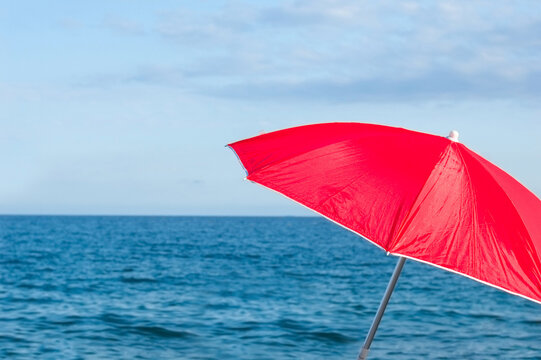 Red parasol umbrella on tropical island beach. Colourful sunshade in the beach on sunny summer day. Holiday relaxation with turquoise sea and blue sky landscape. Summer vacation travel concept