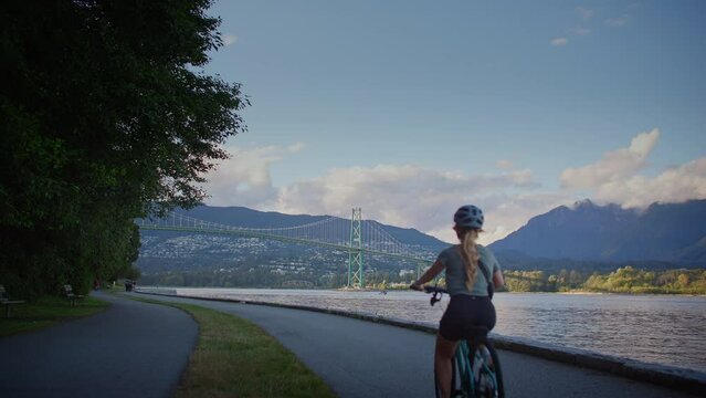Girl biking along the seawall trail with lions gate bridge in background, vancouver