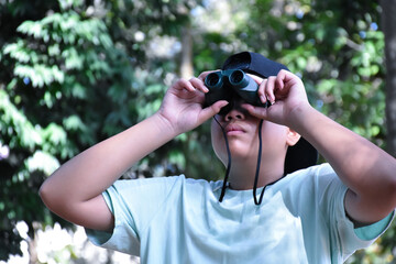 Asian boys are using binoculars to do the birds' watching in tropical forest during summer camp, idea for learning creatures and wildlife animals and insects outside the classroom.