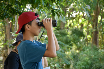 Fototapeta premium Asian boys are using binoculars to do the birds' watching in tropical forest during summer camp, idea for learning creatures and wildlife animals and insects outside the classroom.