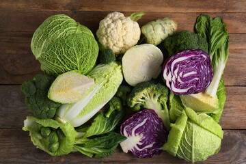 Different whole and cut types of cabbage on wooden table, flat lay