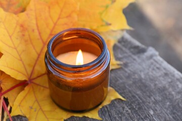 Obraz na płótnie Canvas Burning candle and beautiful dry leaves on wooden surface outdoors, closeup with space for text. Autumn atmosphere