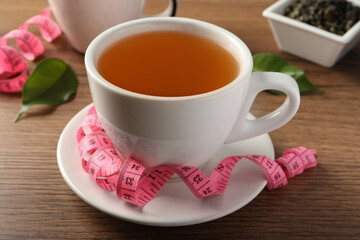Fototapeta premium Cup of herbal diet tea and measuring tape on wooden table. Weight loss concept
