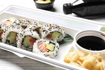 Food delivery. Delicious sushi rolls, soy sauce and ginger in plastic container on table, closeup