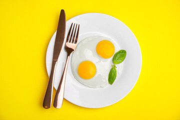 Tasty fried eggs with basil in plate on yellow background, top view